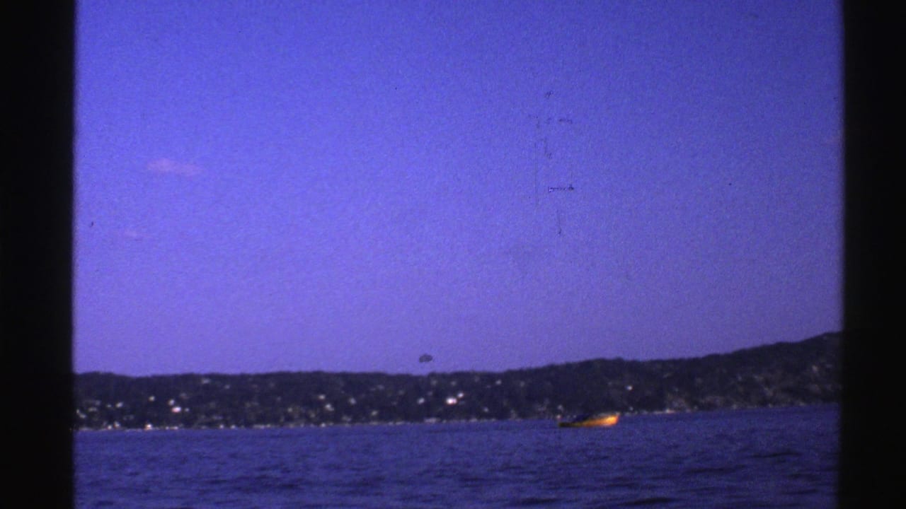 1976 Norway 8mm frame with a small yellow boat near a dark shoreline beneath a blue sky.