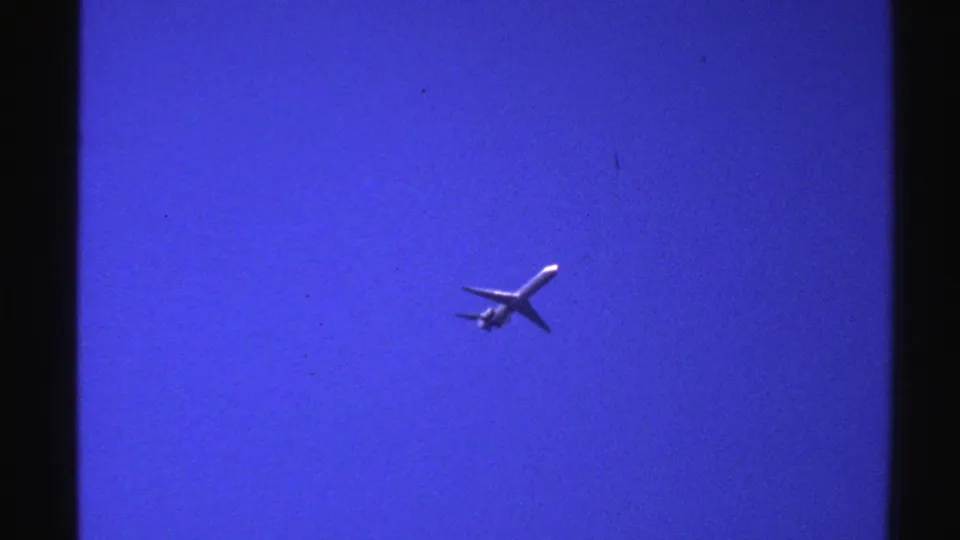 1976 Norway 8mm frame with an airplane in blue sky, bordered by dark contact-sheet frame edges.