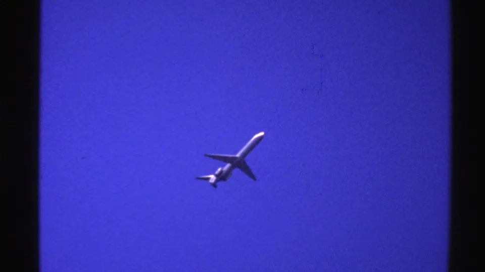 1976 Norway 8mm frame showing the airplane from below as it continues across an empty blue sky.