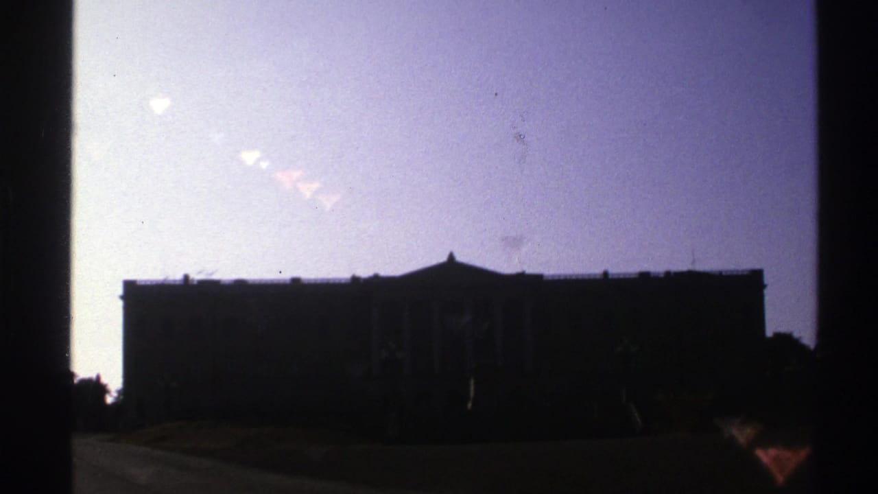 A large classical-style exterior appears in silhouette under a bright pale sky in Norway-sourced 1976 8mm footage.