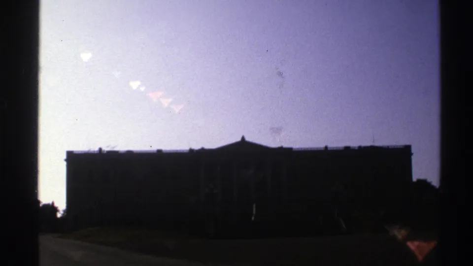 A large classical-style exterior appears in silhouette under a bright pale sky in Norway-sourced 1976 8mm footage.