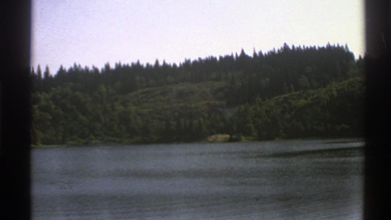 Lake bordered by forested hills, seen through dark 8mm frame edges.