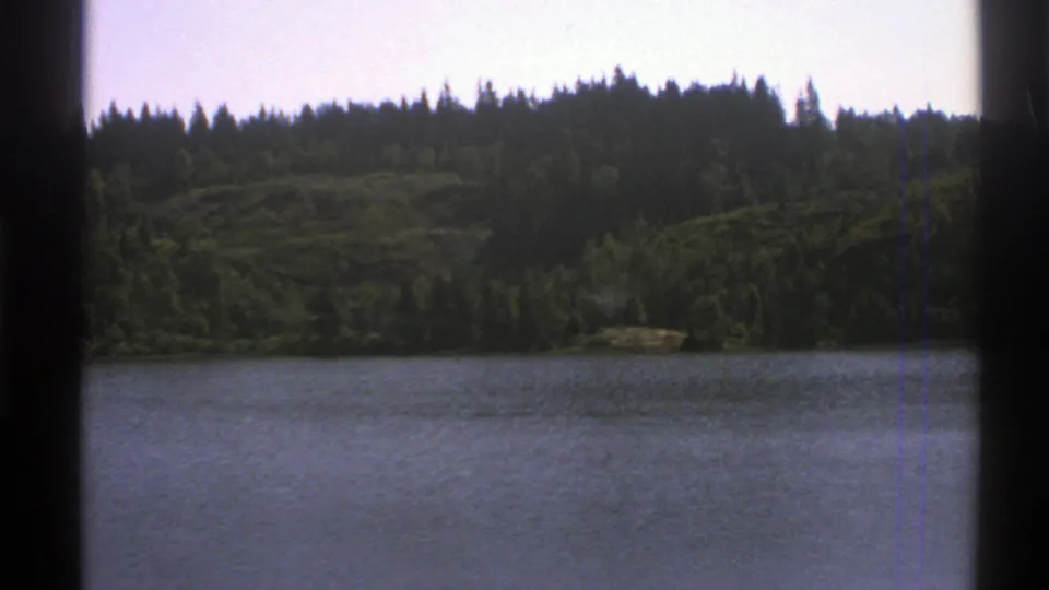1976 Norway 8mm view of water, forested hills, and dark vertical frame edges from the scanned film.