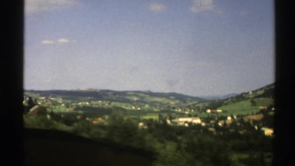 1976 Norway 8mm frame of rolling green fields, distant houses, low hills, and a bright sky.