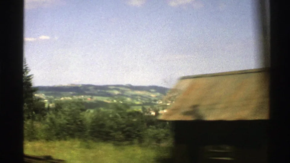 1976 Norway 8mm frame showing rolling countryside, scattered houses, and a passing country building at right.