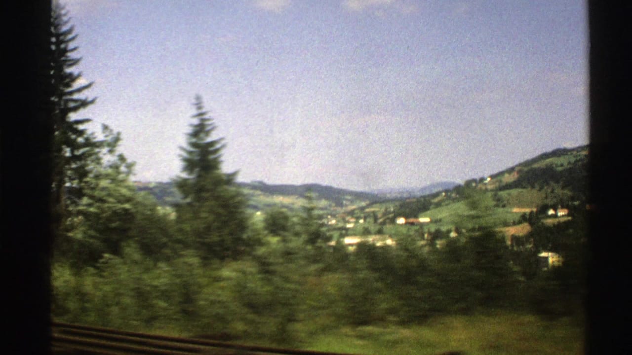 1976 Norway 8mm view of green hills, scattered houses, and conifer trees passing outside a train window.