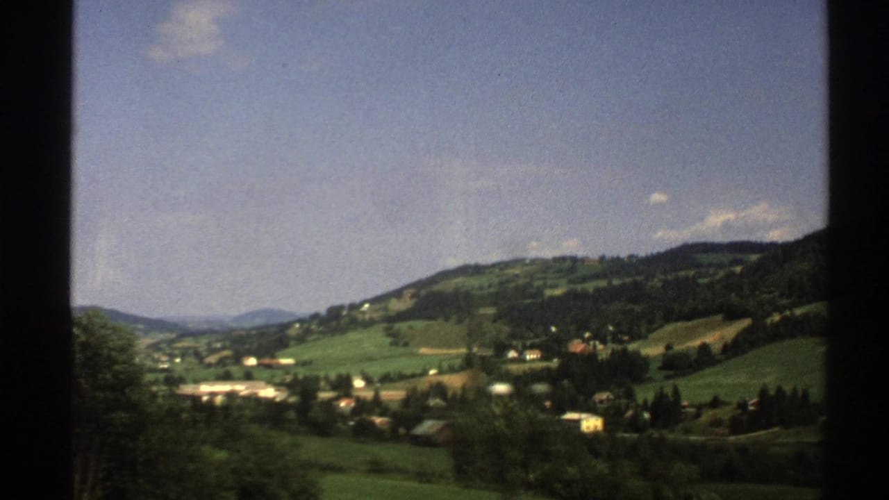 Rolling hills and small buildings seen through dark train-window borders.
