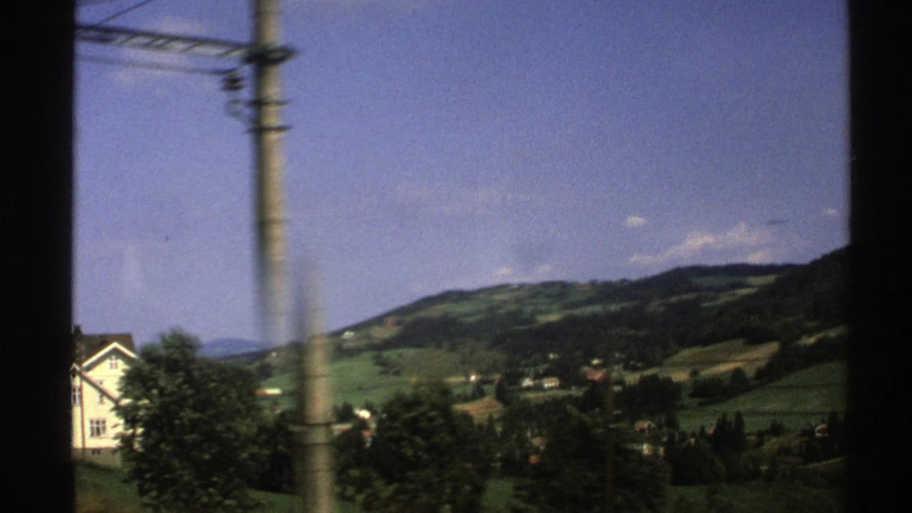 Roadside view of a white house, utility pole, green hills, trees, and blue sky.