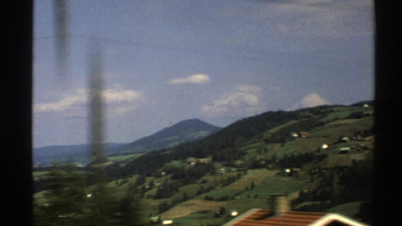 Green hills and valley landscape with scattered houses beneath a blue sky.