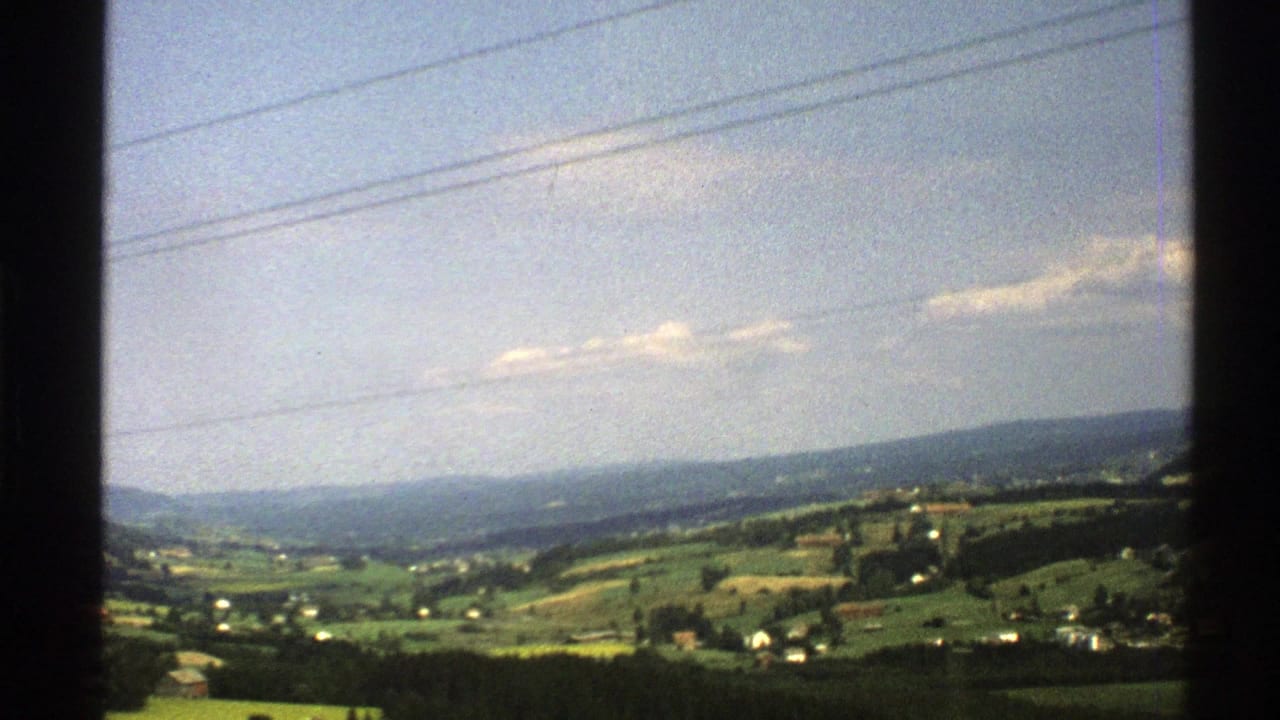 1976 Norway home-movie view of rolling farmland and distant hills, framed by a vehicle window with overhead utility lines.