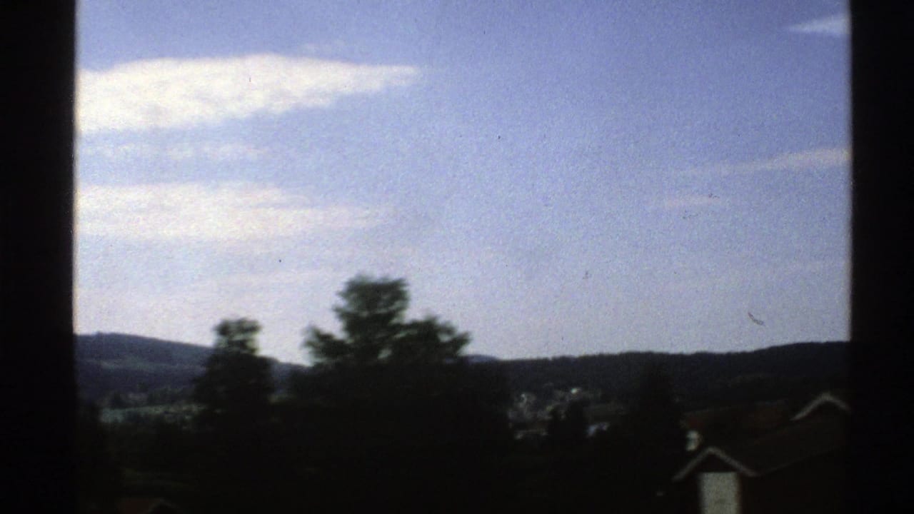Trees and hills beneath a blue sky, with dark window framing at the sides.