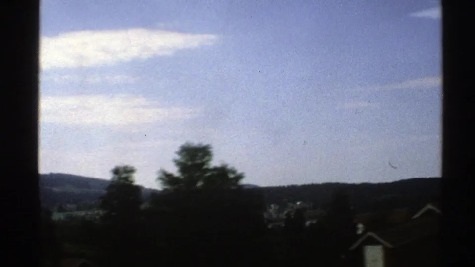 Moving 8mm view in Norway with tree silhouettes, distant ridgeline, blue sky, and window edges in the foreground.