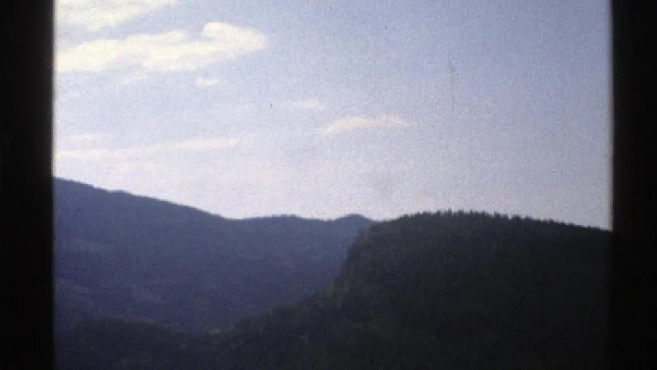 1976 Norway 8mm travel view of dark forested hills and distant ridges beneath a bright clouded sky, framed by a vertical dark edge.