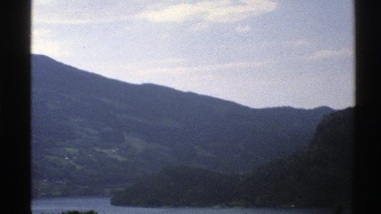 Mountain slopes and a waterway appear beyond a dark window frame.