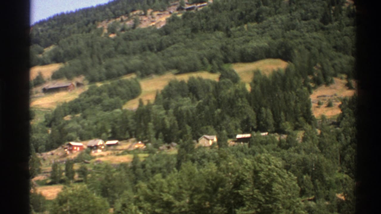 Forested Norwegian hillside with scattered homes and fields seen through dark frame edges.