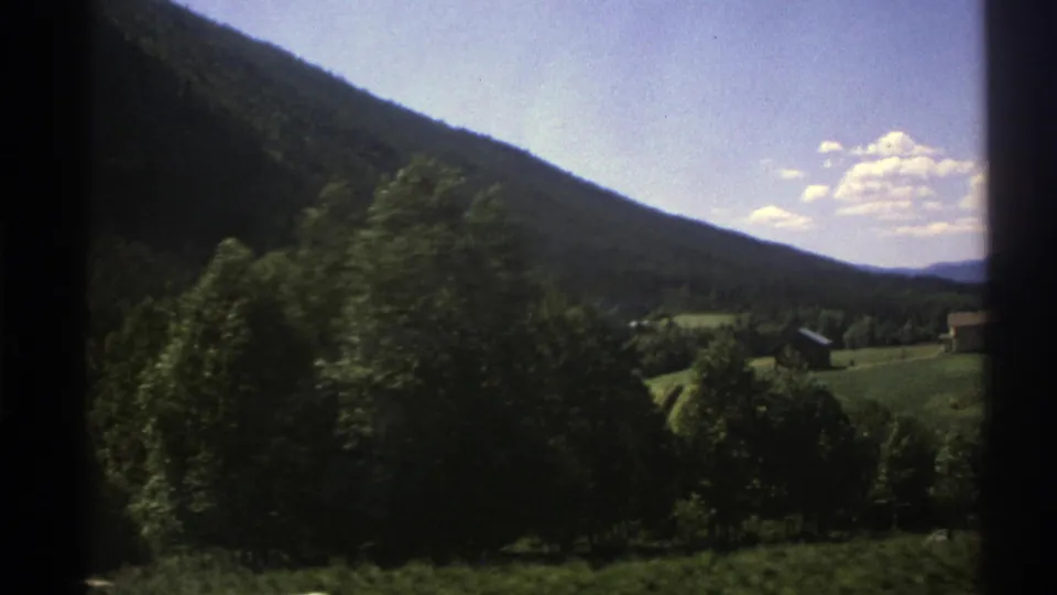 1976 Norway home-movie view of a wooded hillside and green valley with small houses, filmed from a moving vehicle.
