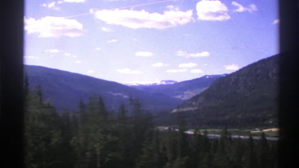 1976 Norway 8mm scenery showing dark forest in the foreground and layered mountain valley views in the distance.