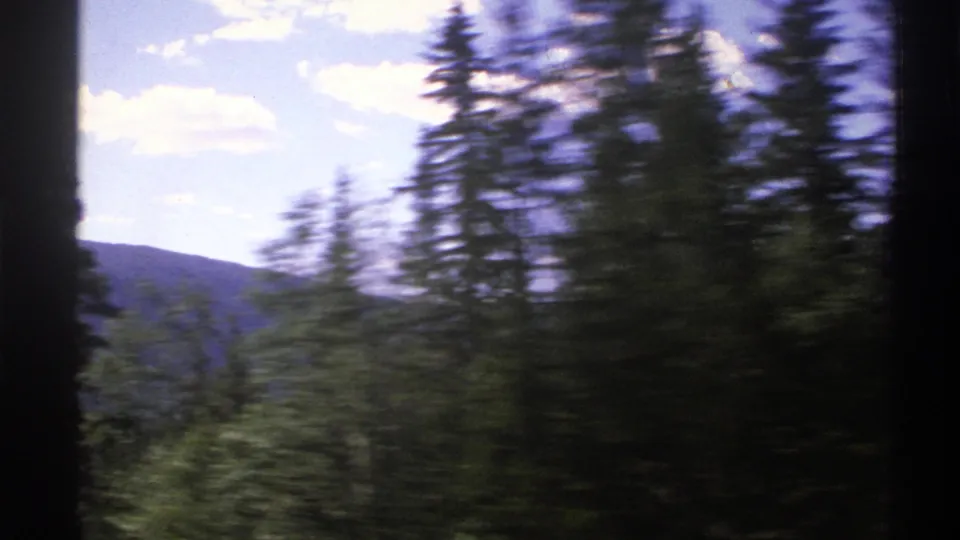 1976 Norway 8mm travel frame with dense green conifers in motion blur and a low mountain ridge beneath scattered clouds.