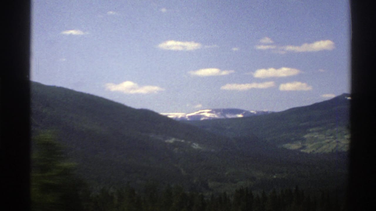Forested mountain valley and distant snow patches framed by dark car-window edges.