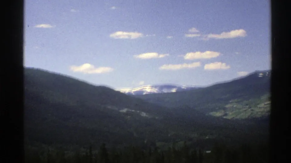 1976 Norway travel footage shows a wide valley and snow-streaked mountains viewed through a vehicle window.