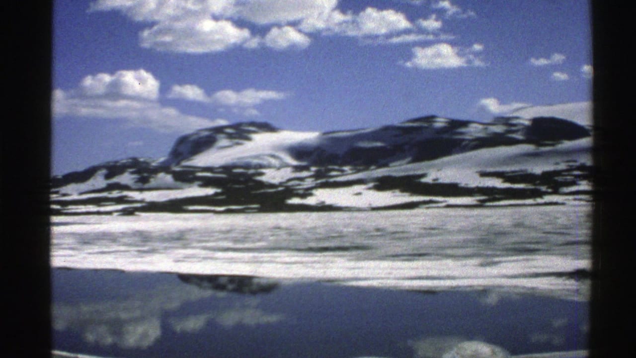 Snow-streaked mountains and clouds reflected in a calm body of water.