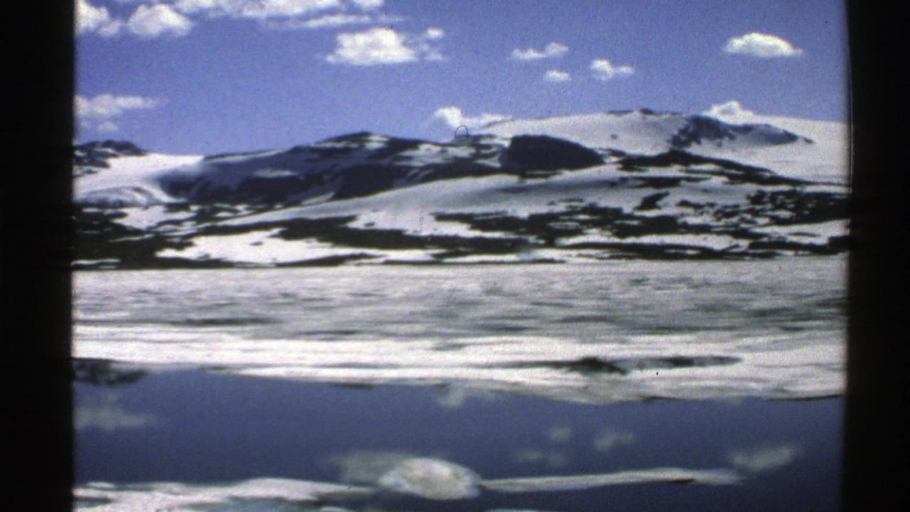 Snowy mountain ridge reflected in calm icy water under a blue sky.