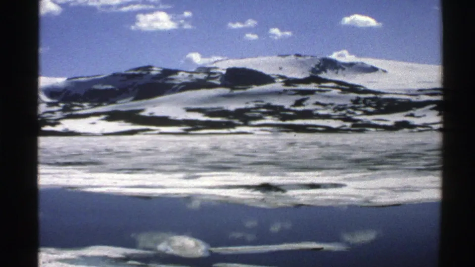 1976 Norway 8mm frame with a snowy ridge, dark rock bands, pale ice or water, and blue sky with clouds.
