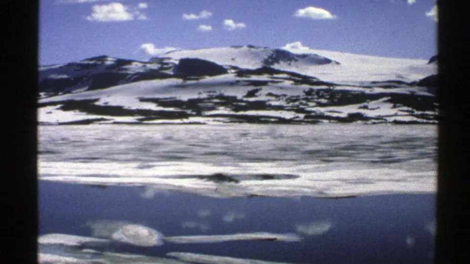 1976 Norway 8mm frame holding on snowfields, exposed dark rock, still water, and cloud reflections.
