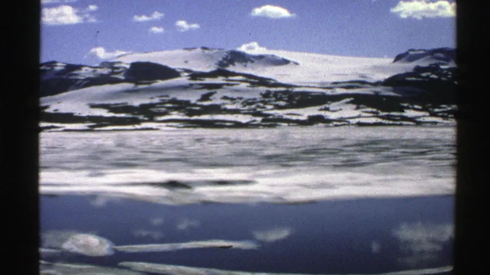 1976 Norway 8mm frame of a snowy mountain and icy water reflection, framed by visible film edges.