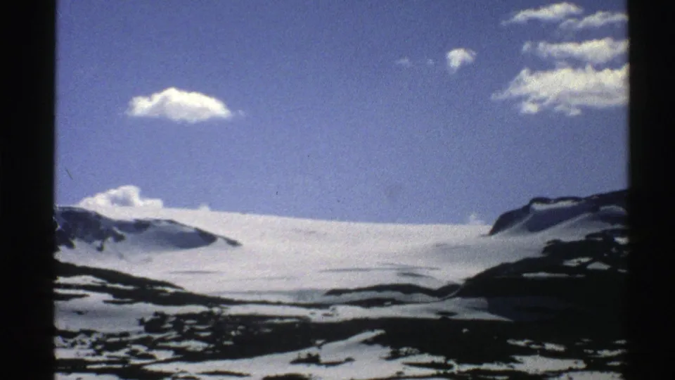 1976 Norway 8mm frame with a steady view of a snowy mountain plateau, dark rock outcrops, and scattered clouds.