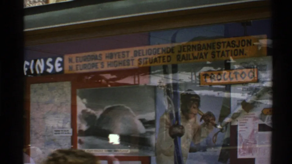 1976 Norway 8mm view of a shop window with railway-station signage, posters, glass reflections, and a partial person at the lower edge.