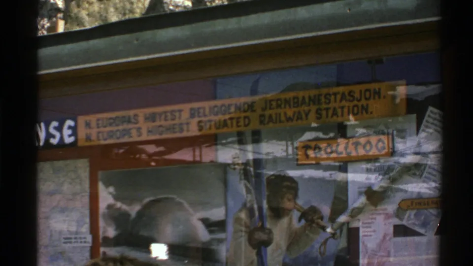 1976 Norway frame showing the window display, bilingual railway-station sign, reflected glass, travel notices, and a monkey poster.