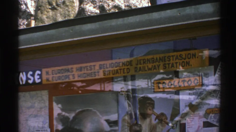 1976 Norway 8mm frame with the railway-station sign partly framed by dark window bars and a chimpanzee poster below.