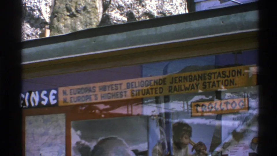 8mm frame of Norwegian railway station signage and poster display, with saturated color and dark window bars.