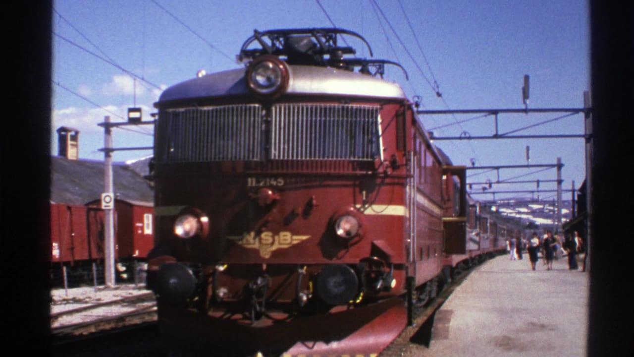 1976 Norway frame of a red NSB locomotive at the platform, viewed from the front with station activity and rail yard elements visible.