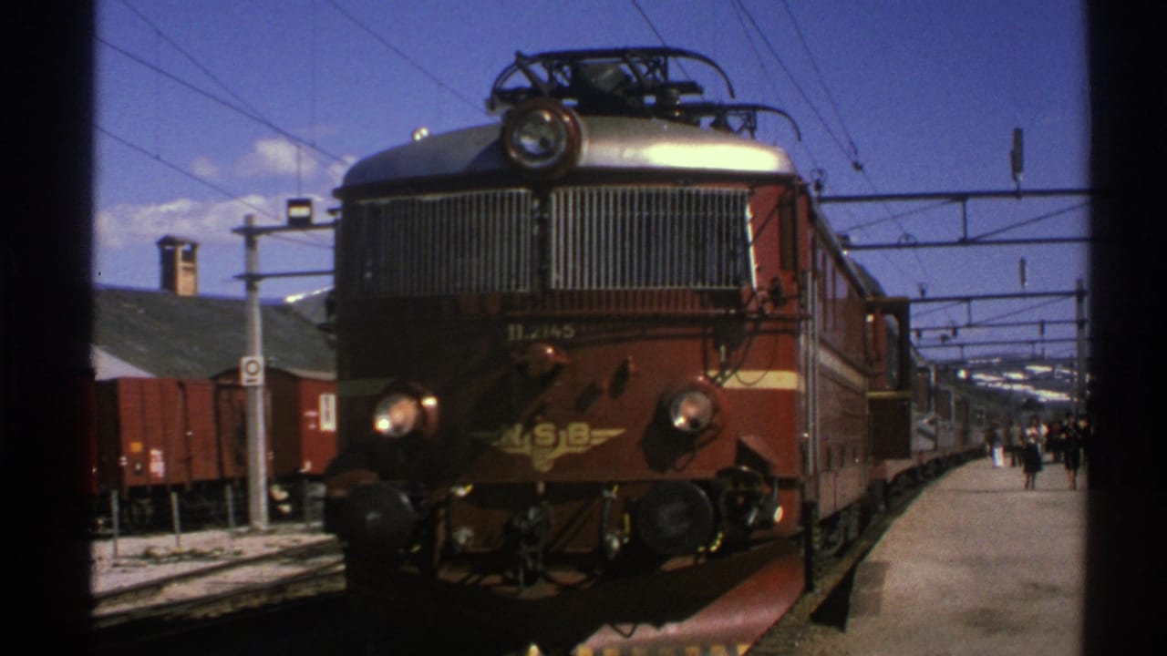 1976 Norway home-movie frame showing a brown and gold NSB electric locomotive at a sunny station platform.
