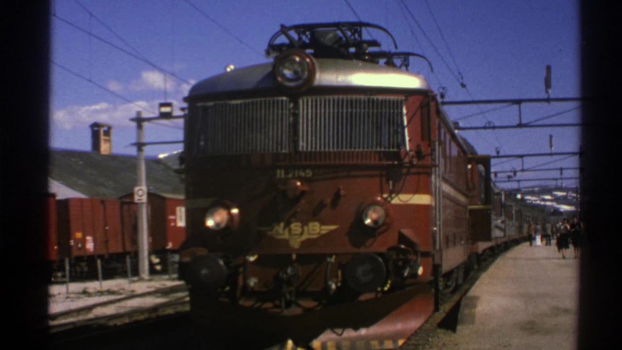 Window-framed 1976 Norway view of an NSB electric locomotive stopped beside a station platform.