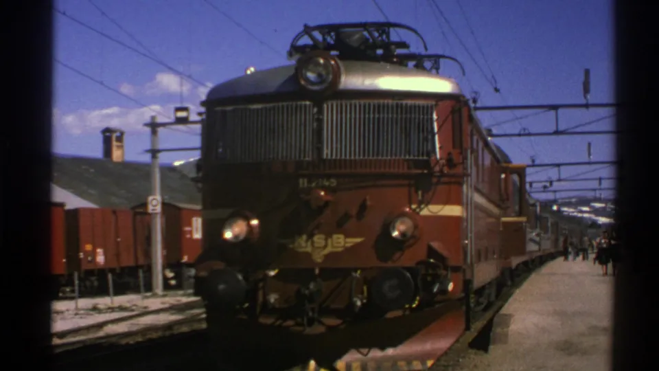Close 1976 Norway station frame with the NSB locomotive front, freight cars, platform, and overhead lines.