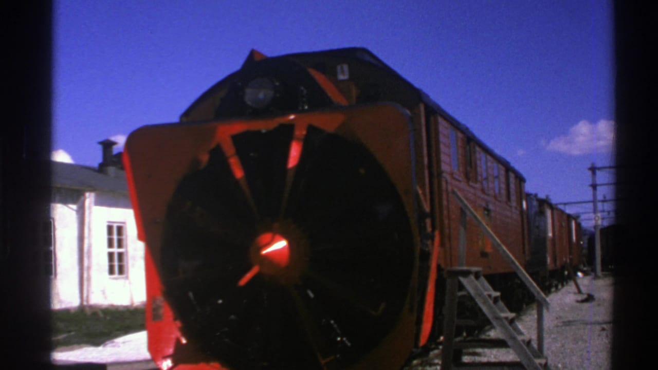 1976 Norway 8mm frame showing a red train with a circular snowplow front stopped at a rural station under blue sky.