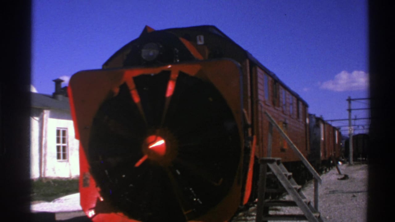 Close trackside view of a red snowplow-front train with cars behind it.