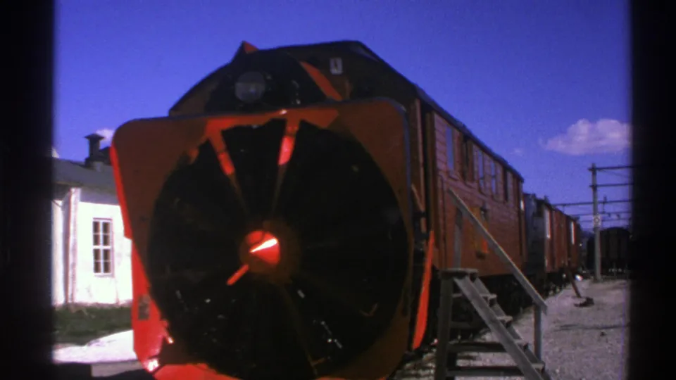 1976 Norway 8mm frame showing the stopped red rail vehicle, circular snowplow attachment, and small station structure at left.