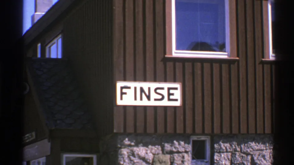 1976 Norway 8mm still of the FINSE sign on a dark wood building with stone foundation and small windows.