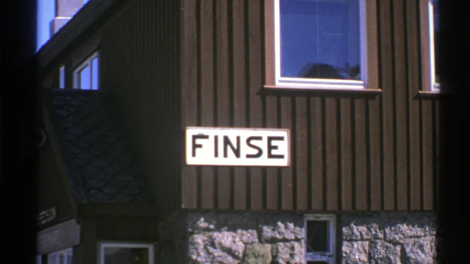 Final 1976 Norway frame holding on the FINSE sign, dark wood siding, stone base, and blue-reflecting window.