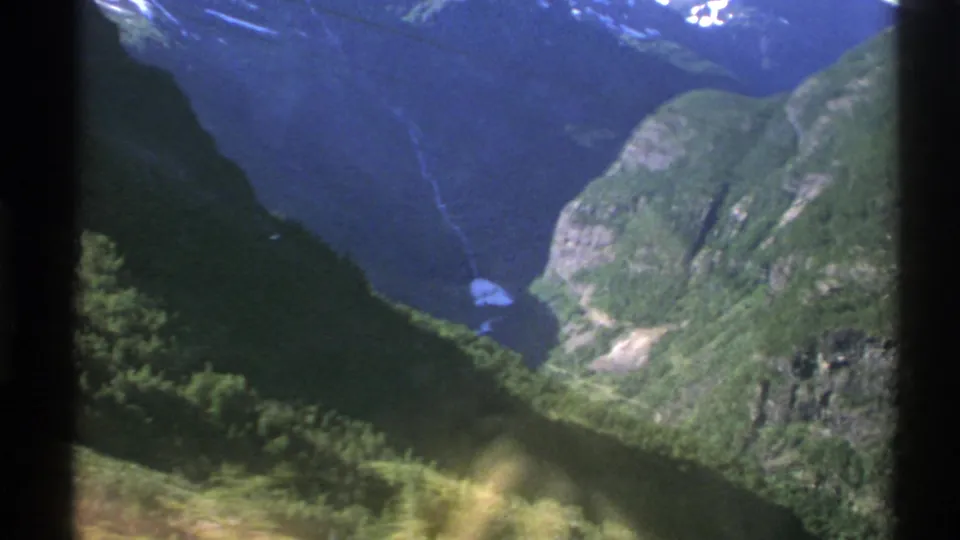 Norwegian mountain and fjord landscape seen from inside transportation, divided by a dark window post.