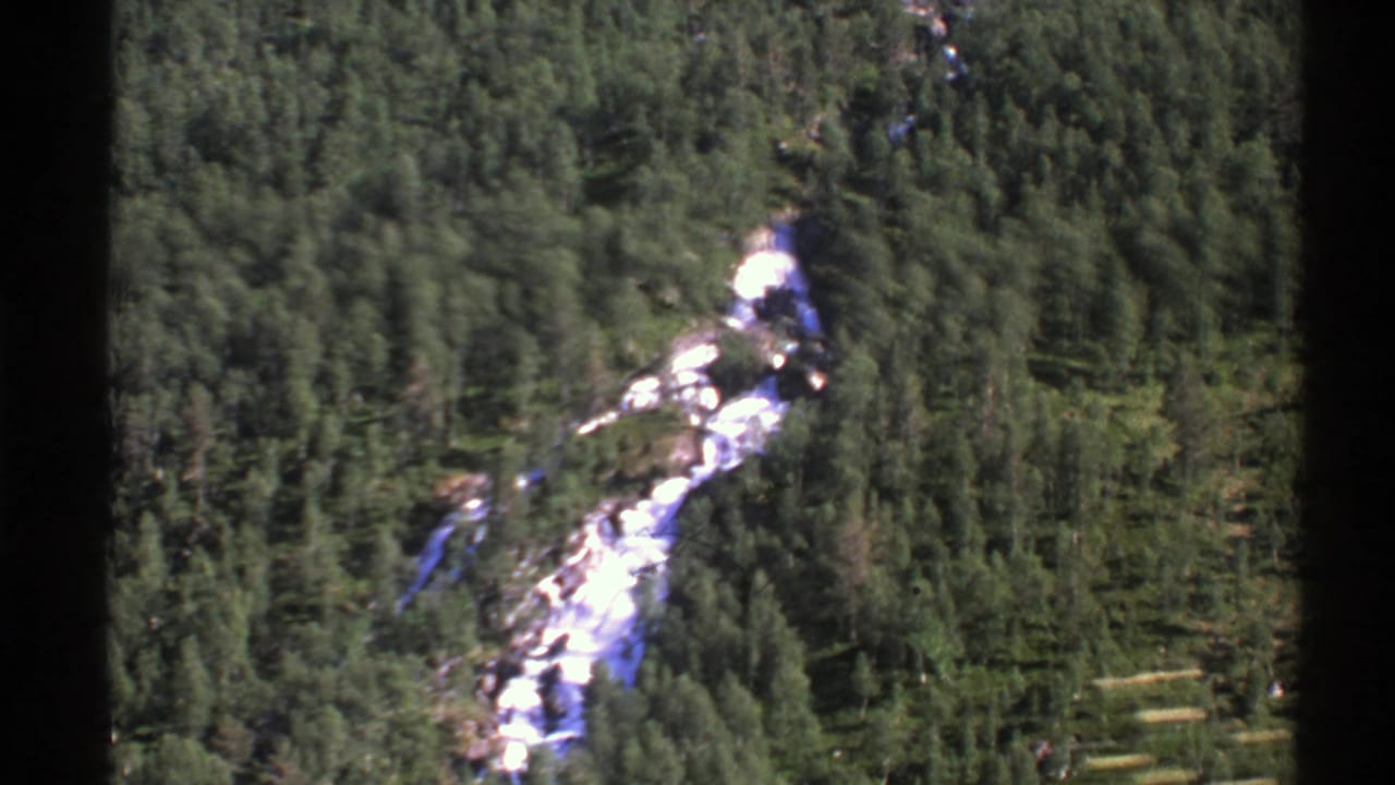 Norwegian mountain forest and a pale river course pass by in a 1976 8mm train-window view.