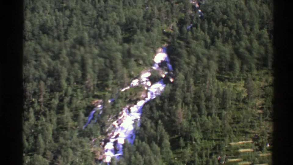 Norwegian mountain forest and a pale river course pass by in a 1976 8mm train-window view.