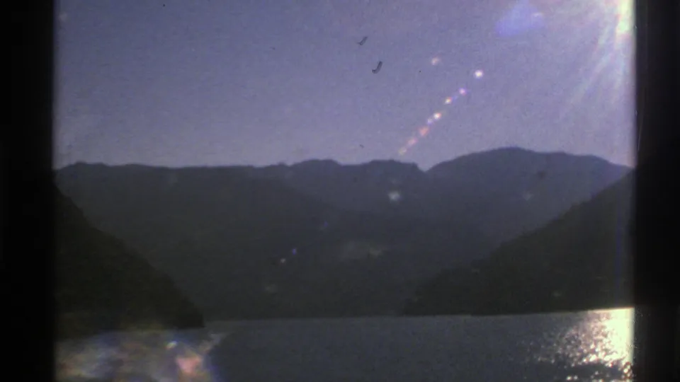 A fjord and layered mountain ridges in Norway appear through train-window framing with flare and reflected light.