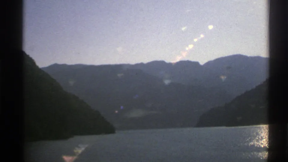 1976 Norway 8mm footage shows a calm fjord between dark mountain slopes with sunlight reflecting on the water.