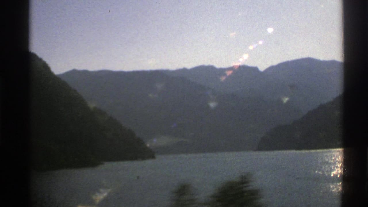 Mountain lake seen through dark frame edges with forested slopes and distant ridges.