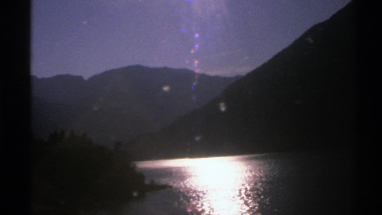 Mountain lake with bright water glare and dark hills on both sides.